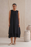 Woman wearing a black sleeveless dress standing in front of textured walls and vases.