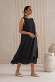 Woman wearing a black sleeveless dress standing in a minimalistic setting with neutral colors.