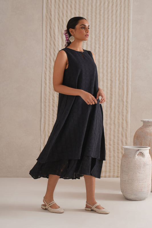 Woman wearing a black sleeveless dress standing in a minimalistic setting with neutral colors.
