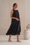 Woman wearing a black sleeveless dress standing in a minimalistic setting with neutral colors.